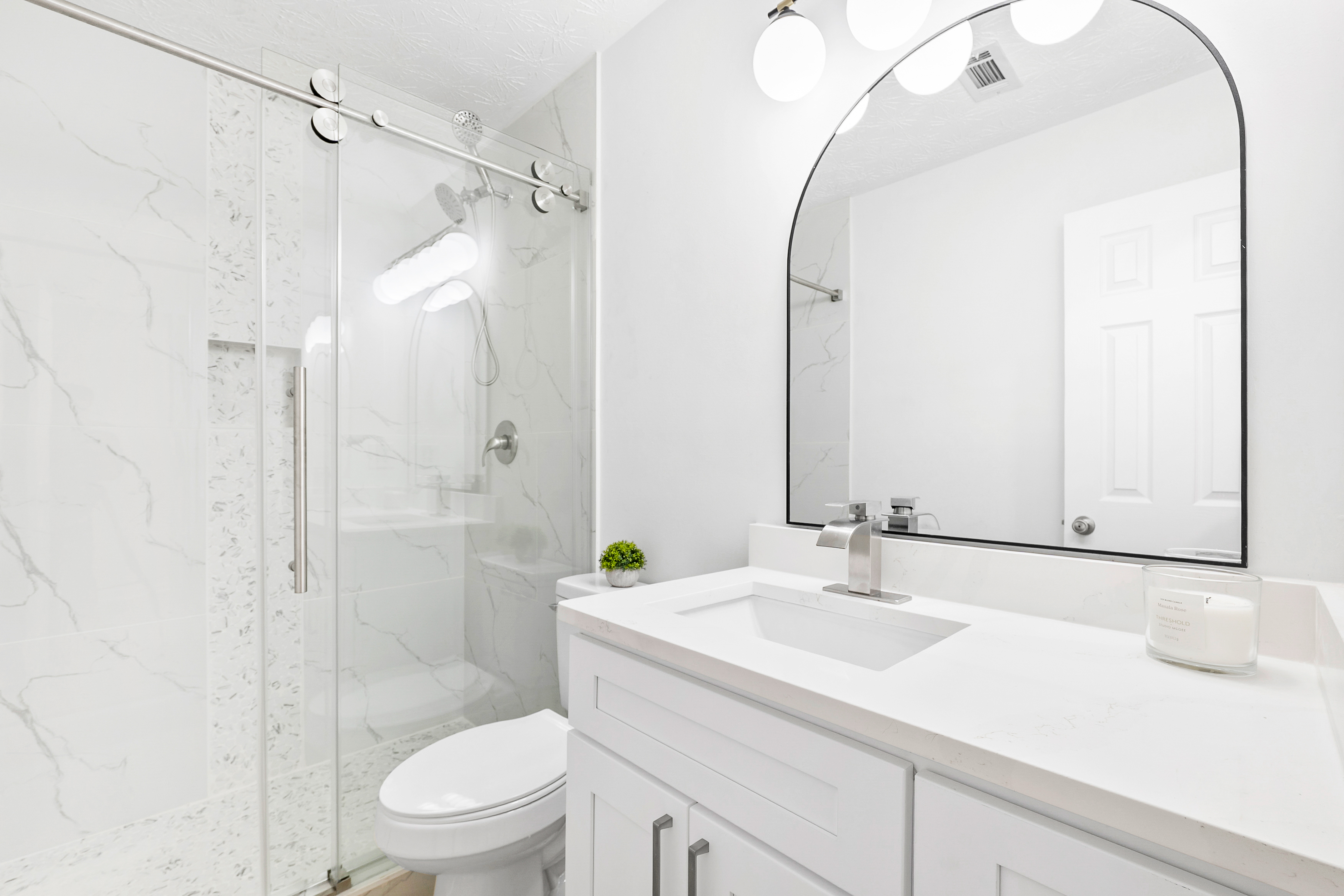 Modern hallway bathroom after remodel with glass shower, marble-look tile, white vanity and black framed mirror