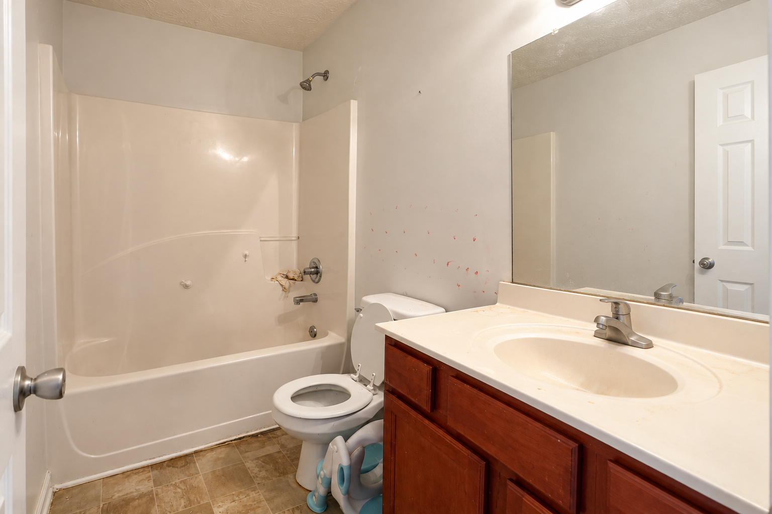 Hallway bathroom before remodel with bathtub, wood vanity, large wall mirror and outdated flooring