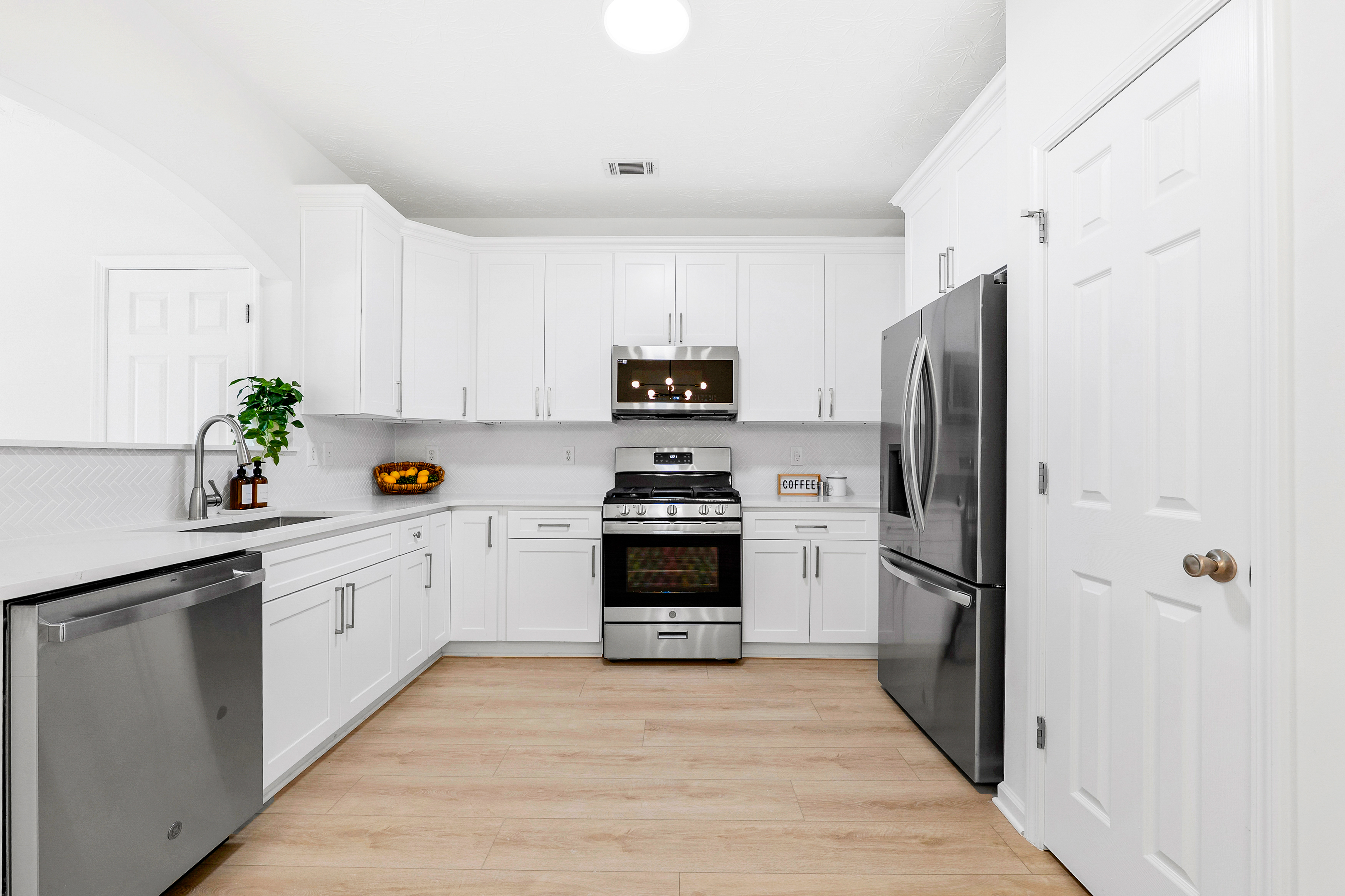Modern kitchen after remodel with white cabinets, new countertops, backsplash, stainless steel appliances and wood-look flooring