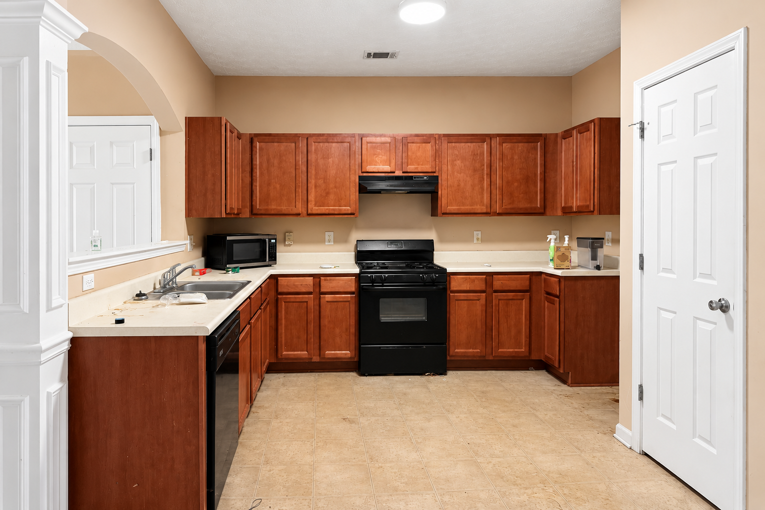 Kitchen before remodel with dark wood cabinets, beige countertops, black appliances and old tile flooring
